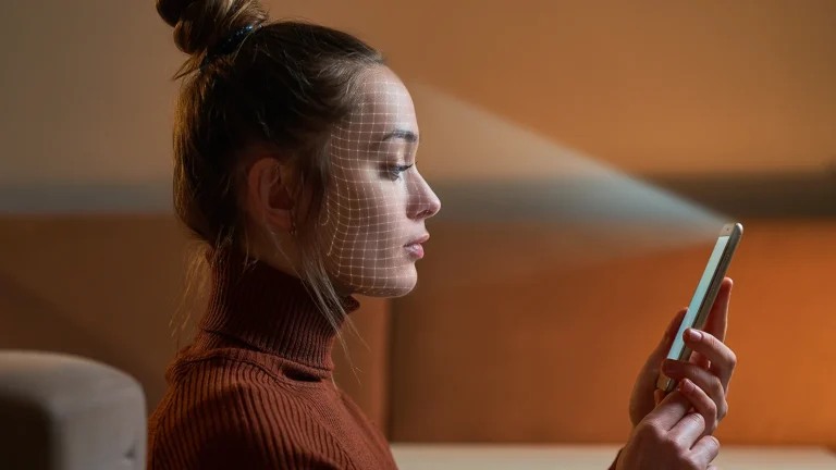 Mulher de perfil olha para um celular, com uma malha digital de reconhecimento facial sobreposta ao rosto.