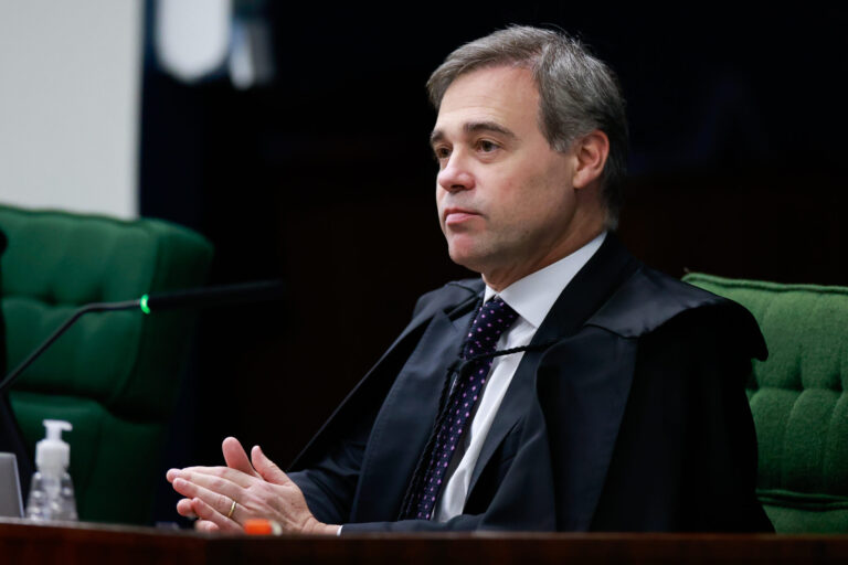 Ministro André Mendonça sentado em uma cadeira verde, usando toga preta e gravata, durante sessão judicial.