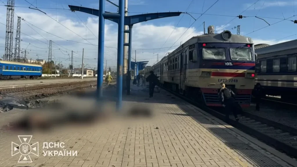 Plataforma ferroviária em Dnipro com trens parados, pessoas próximas aos vagões e áreas desfocadas em primeiro plano.