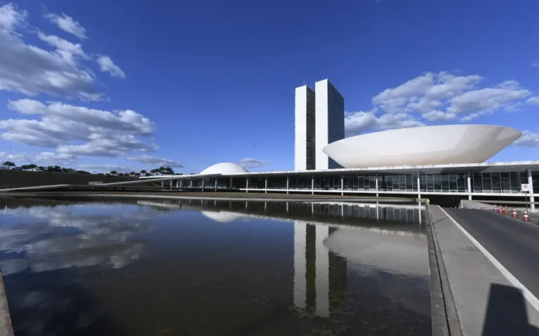 Vista do Congresso Nacional, em Brasília, com as duas cúpulas, as torres centrais e o reflexo dos edifícios no espelho d’água.