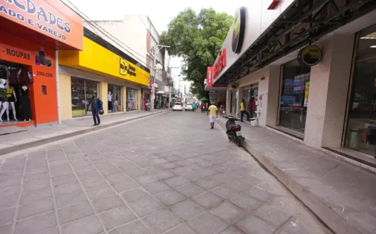 Rua comercial do Centro de Teresina, com lojas dos dois lados, pedestres, veículos ao fundo e uma motocicleta estacionada na calçada.