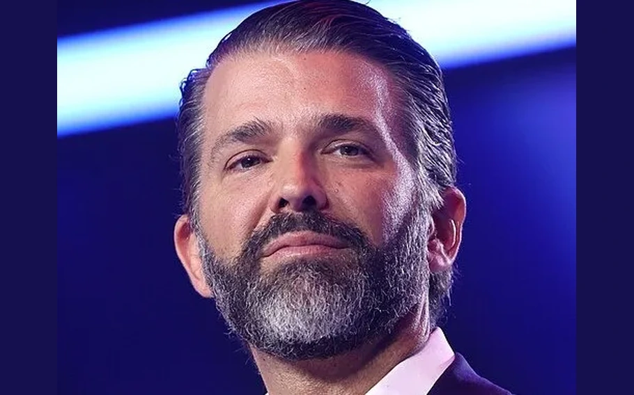 Retrato de Donald Trump Jr., com barba e cabelos penteados para trás, diante de fundo azul.