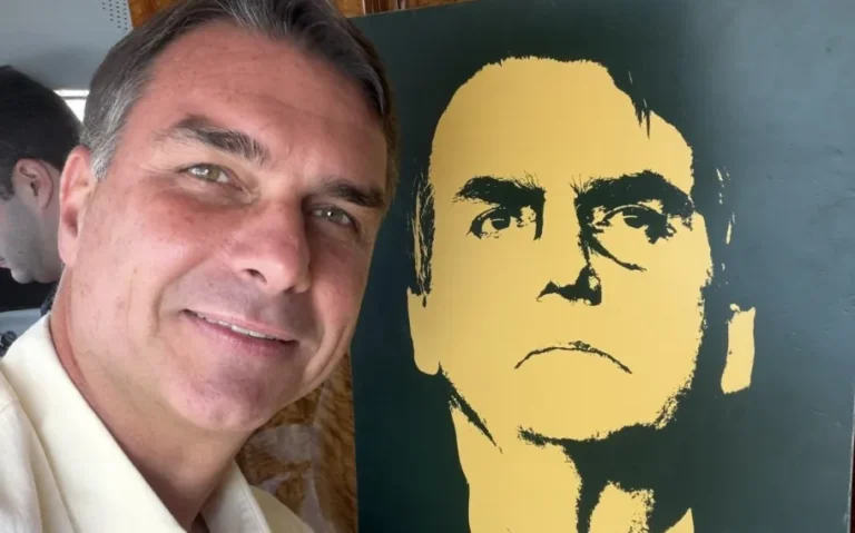 Flávio Bolsonaro durante visita ao Vale do Paraíba, ao lado de uma ilustração do ex-presidente Jair Bolsonaro.