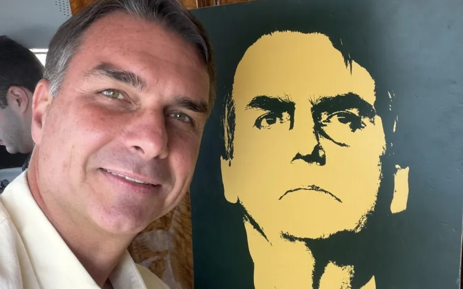 Flávio Bolsonaro durante visita ao Vale do Paraíba, ao lado de uma ilustração do ex-presidente Jair Bolsonaro.