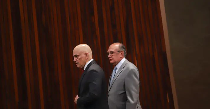 Alexandre de Moraes e Gilmar Mendes caminhando lado a lado em ambiente interno.