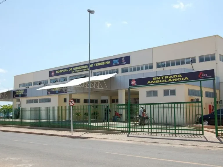 Fachada do Hospital de Urgência de Teresina, com placas de identificação, entrada de ambulâncias, portões verdes e calçada em frente ao prédio.
