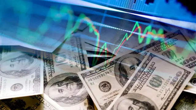 Cédulas de cem dólares americanos sobrepostas por um gráfico financeiro com linhas verdes e vermelhas que representam oscilações do mercado.