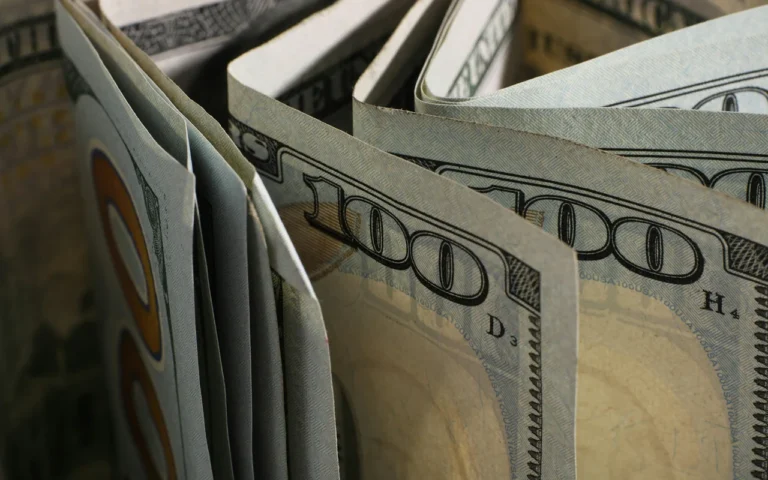 Cédulas de 100 dólares fotografadas em close-up, ilustrando a movimentação do câmbio e a queda do dólar.