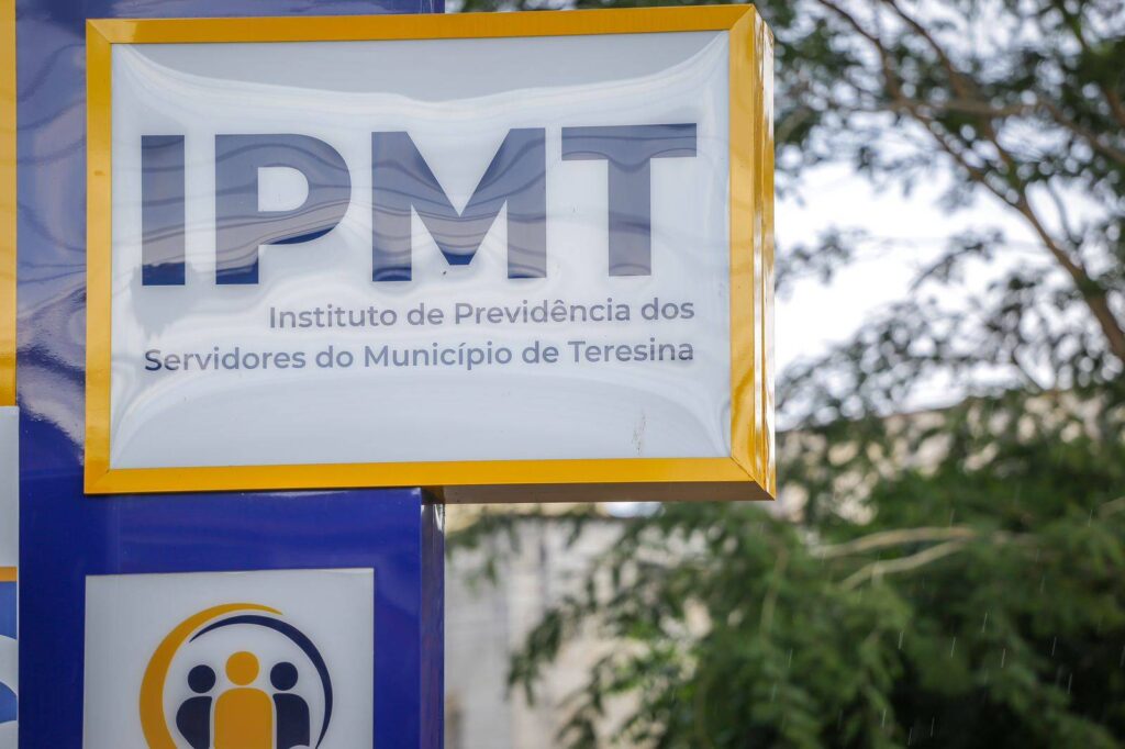 Placa de identificação do IPMT em Teresina, com moldura amarela, logomarca institucional e árvores desfocadas ao fundo.