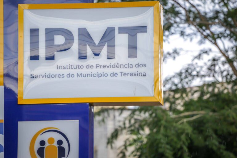 Placa de identificação do IPMT em Teresina, com moldura amarela, logomarca institucional e árvores desfocadas ao fundo.