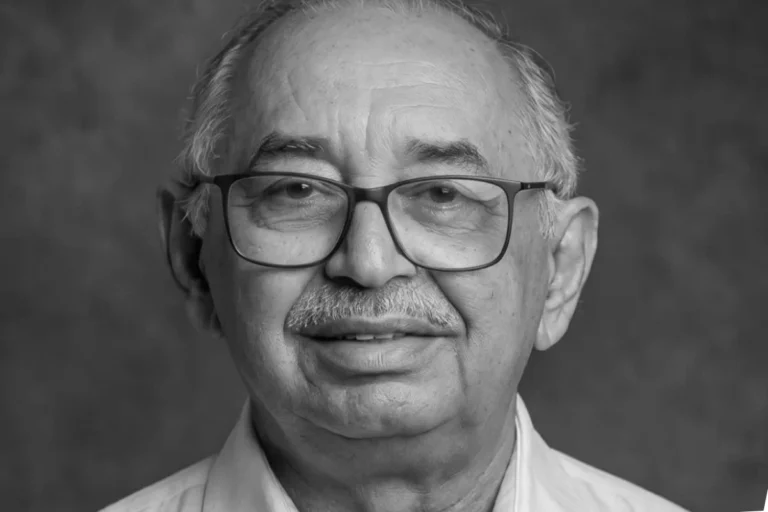 Retrato em preto e branco de José Antônio Coelho, com cabelos grisalhos, óculos de armação escura, bigode e camisa clara.