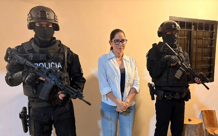 Luisa González, de camisa branca e óculos, entre dois policiais armados de uniforme preto e rosto coberto.