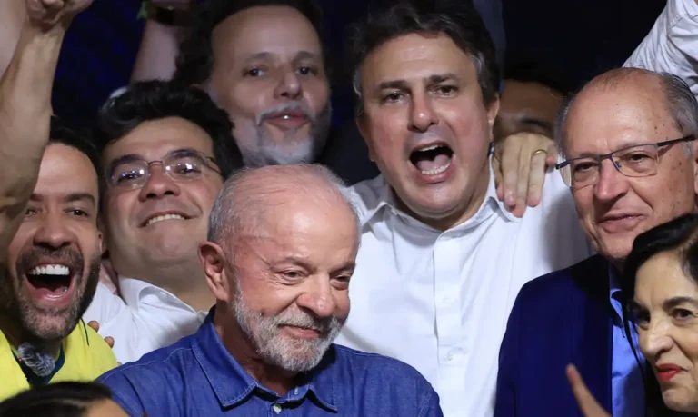 Lula, de camisa azul, aparece cercado por pessoas sorrindo e comemorando.