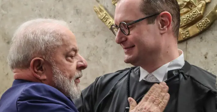 Lula, de terno azul, coloca a mão sobre o peito de Cristiano Zanin, que usa óculos e toga preta.