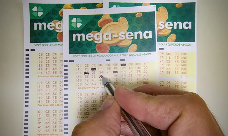 Mão segurando uma caneta e marcando números em um volante da Mega-Sena, com outros bilhetes da loteria ao fundo.