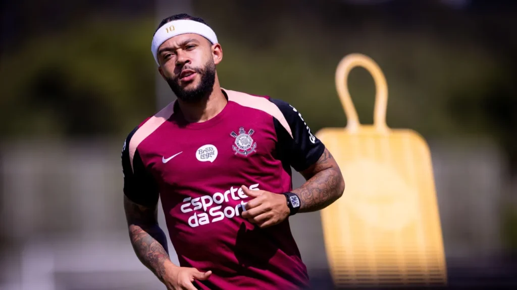 Memphis Depay corre durante treino do Corinthians, usando camisa bordô do clube e faixa branca na cabeça.