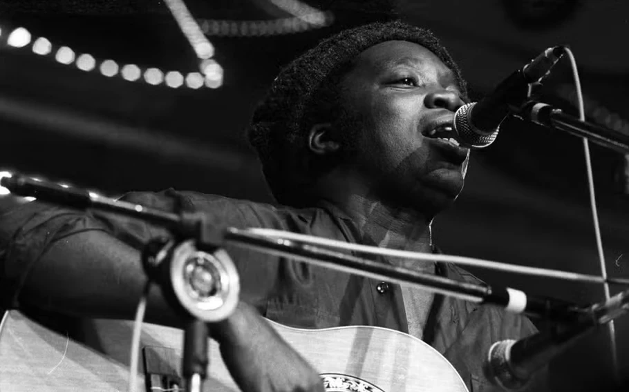 Milton Nascimento canta ao microfone e toca violão durante apresentação em 1978, em fotografia em preto e branco.