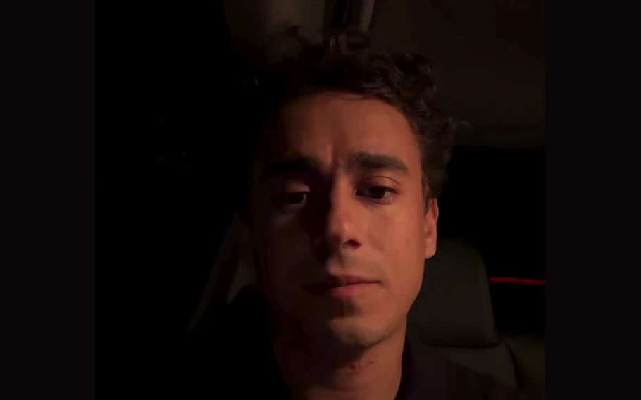 Nikolas Ferreira aparece dentro de um veículo, vestindo camisa escura, durante gravação em ambiente pouco iluminado.