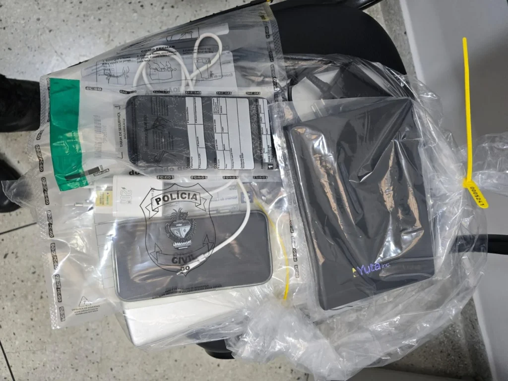 Objetos e aparelhos eletrônicos acondicionados em sacos plásticos de evidências policiais sobre uma cadeira preta, com celular, cabos brancos e identificação da Polícia Civil de Goiás.