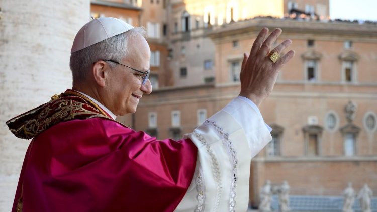 Papa Leão XIV usando vestes brancas e óculos, acenando na varanda do Vaticano.