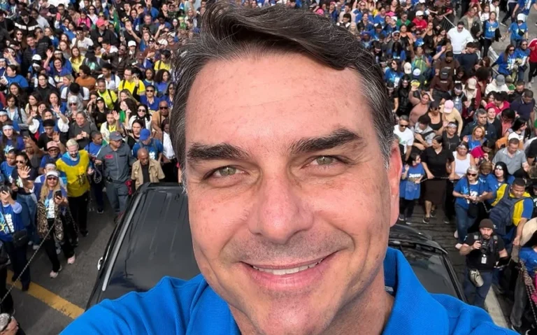 Flávio Bolsonaro, de camisa polo azul, faz selfie diante de uma multidão que ocupa uma rua.