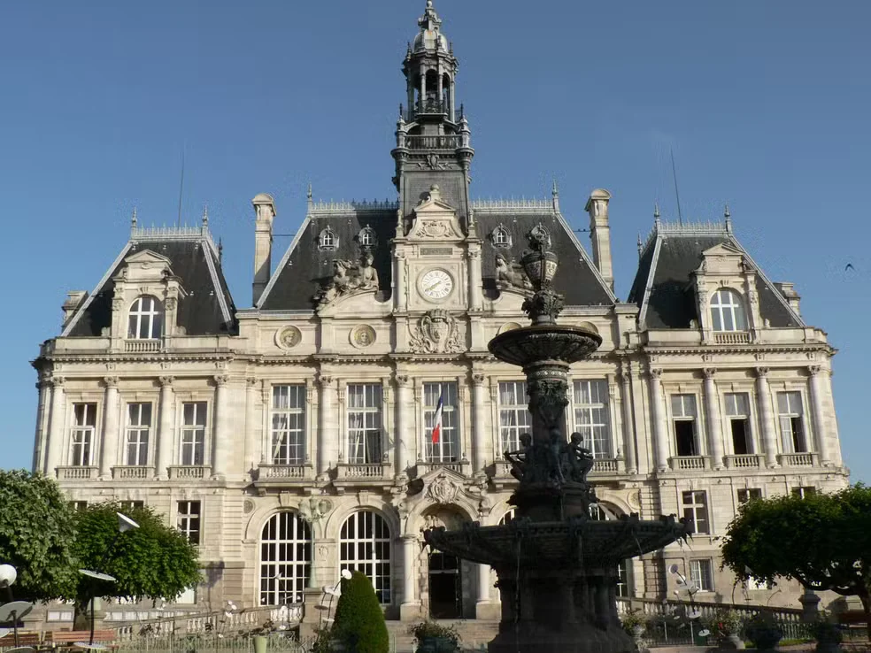 Fachada histórica da prefeitura de Limoges, com torre do relógio, telhados escuros e fonte ornamental à frente.