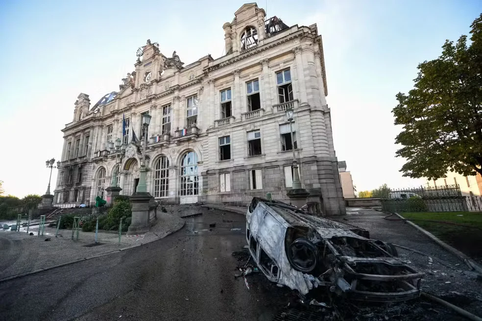 Carro carbonizado sobre o pavimento diante da prefeitura de Limoges, com danos no telhado do edifício ao fundo.