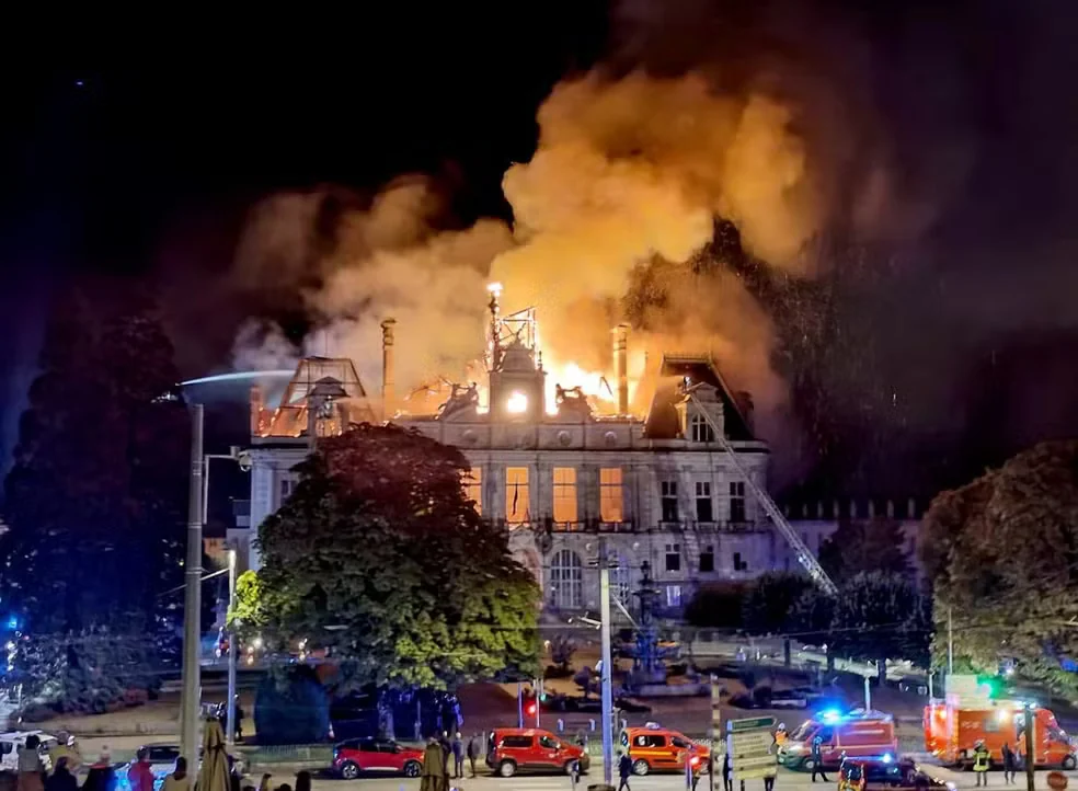 Fumaça e chamas sobre o telhado da prefeitura de Limoges, com veículos de bombeiros e equipes de emergência na praça.