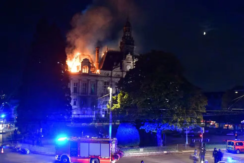 Incêndio em parte do telhado da prefeitura de Limoges à noite, com fumaça e luzes de viaturas de bombeiros.