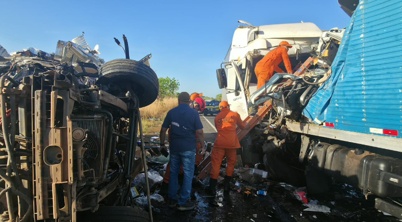 Equipes de resgate com uniformes laranja trabalham entre um caminhão tombado, à esquerda, e caminhões com cabines destruídas, à direita.