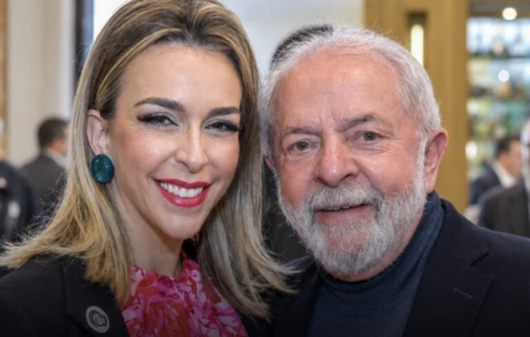 Roberta Luchsinger sorri ao lado de Lula. Ela veste blazer preto e roupa rosa; o presidente usa paletó escuro e blusa azul-marinho.