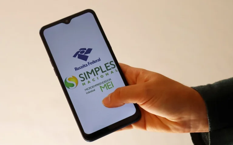 Mão segura celular com os logotipos da Receita Federal, do Simples Nacional e do MEI na tela.