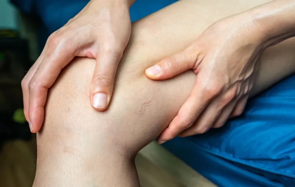 Pessoa sentada segura a perna com as duas mãos na região do joelho.