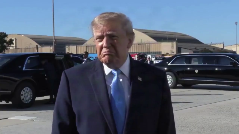 Donald Trump, de terno escuro e gravata azul, fala à imprensa em área externa, diante de veículos oficiais.